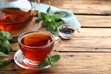 Photo of Cup of aromatic black tea with fresh mint on wooden table. Space for text