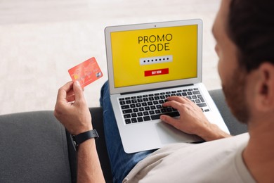 Photo of Man holding laptop with activated promo code and credit card on sofa, closeup
