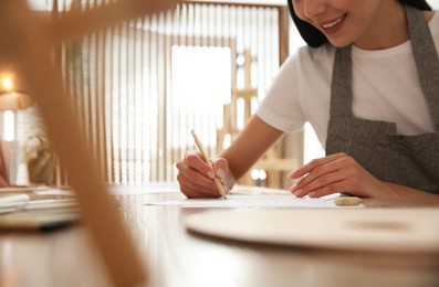 Photo of Young woman drawing with pencil at table indoors, closeup