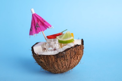 Summer refreshing cocktail with umbrella in coconut on color background