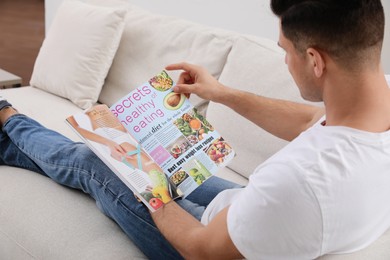 Man reading on sofa in living room, focus on magazine