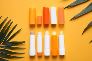 Sun protection lip balms and leaves on orange background, flat lay