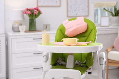 High chair with set of baby tableware on tray indoors
