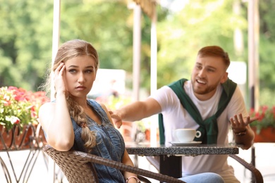 Young couple arguing while sitting in cafe, outdoors. Problems in relationship