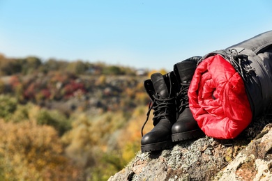 Boots and sleeping bag on rock outdoors, space for text. Camping equipment
