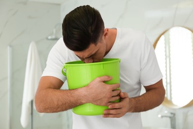 Man with bucket suffering from nausea in bathroom. Food poisoning