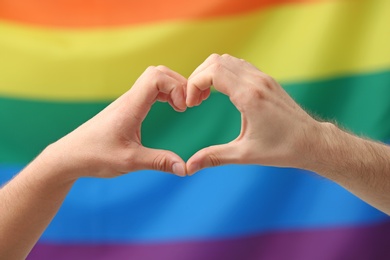 Gay couple making heart symbol with hands on rainbow background. Sexual minority