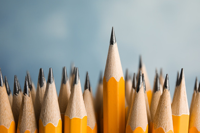 Many graphite pencils and one standing out on blue background, closeup