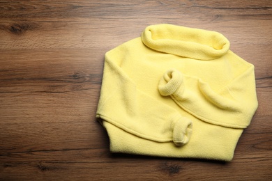 Photo of Yellow warm sweater on wooden table, top view. Space for text