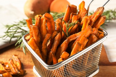 Frying basket with sweet potato fries and rosemary on wooden table, closeup