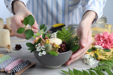 Photo of Closeup view of woman making floral composition with candle at wooden table. Master class