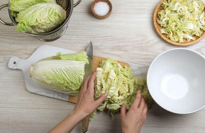 Woman cutting Chinese cabbage at white wooden kitchen table, top view