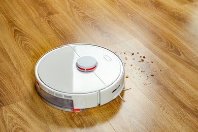 Robotic vacuum cleaner removing dirt from wooden floor indoors, space for text