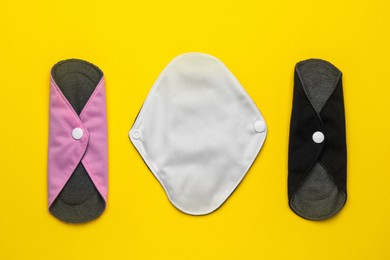 Reusable cloth menstrual pads on yellow background, flat lay