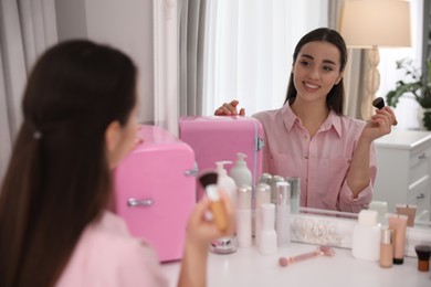 Woman getting ready at dressing table with cosmetic fridge indoors