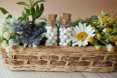 Bottles with homeopathic remedy and flowers in basket on wooden table, closeup