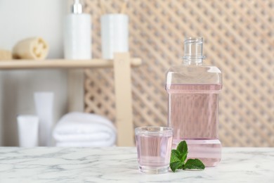 Bottle and glass with mouthwash on white marble table in bathroom, space for text