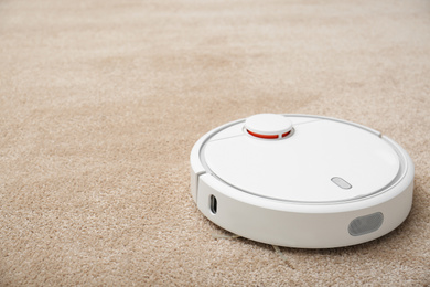 Photo of Removing dirt from carpet with modern robotic vacuum cleaner indoors. Space for text