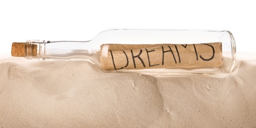 Corked glass bottle with Dreams note on sand against white background