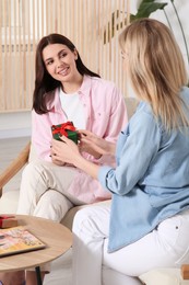 Photo of Smiling young woman presenting gift to her friend at home