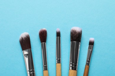 Different makeup brushes on light blue background, flat lay. Space for text