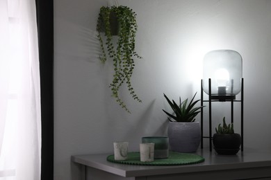Stylish lamp, candles and green plants on grey table indoors. Interior design