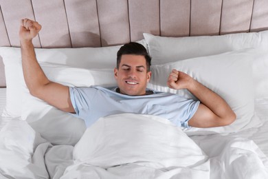 Man awakening in comfortable bed with white linens, above view