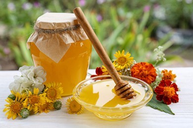 Delicious honey and dipper with different flowers on white wooden table in garden