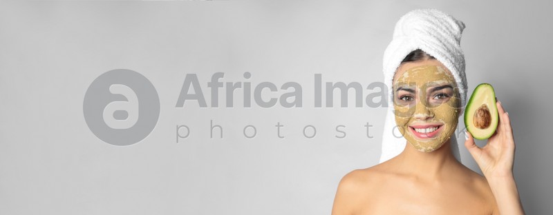 Young woman with clay mask on her face holding avocado against light background, space for text. Banner design