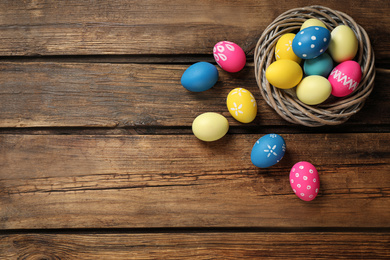 Colorful Easter eggs in decorative nest on wooden background, flat lay. Space for text