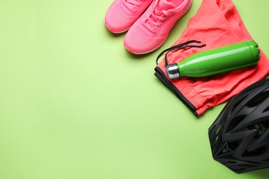 Flat lay composition with different cycling accessories and clothes on green background, space for text