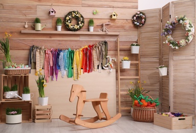Stylish Easter photo zone with flower wreaths, rocking horse and houseplants