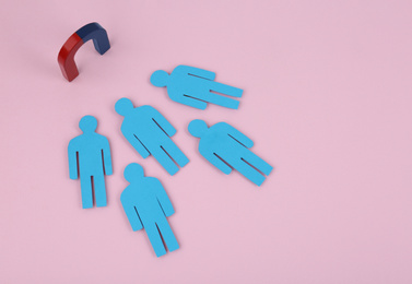 Magnet attracting paper people on pink background, above view