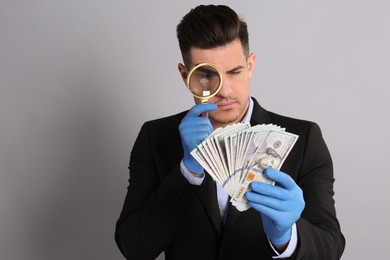 Photo of Expert authenticating 100 dollar banknotes with magnifying glass on light grey background. Fake money concept