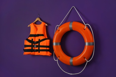 Orange life jacket and lifebuoy on violet background. Rescue equipment