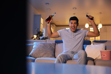 Man watching movie with popcorn and bottle of beer on sofa at night