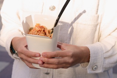 Photo of Woman holding paper box of takeaway noodles with fork, closeup. Street food