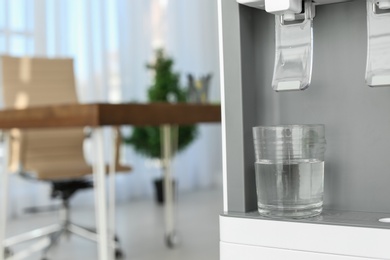 Modern water cooler with glass in office, closeup. Space for text
