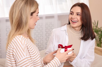 Photo of Smiling young woman presenting gift to her friend at home