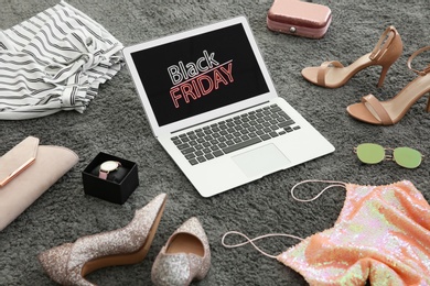 Laptop with Black Friday announcement surrounded by clothes and accessories on grey carpet