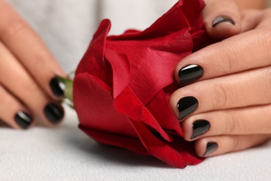 Woman with black manicure holding rose at table, closeup. Nail polish trends
