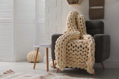 Photo of Comfortable armchair with chunky knit blanket in light living room