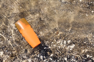 Bottle with sun protection spray on seashore, top view. Space for text