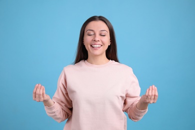 Young woman meditating on light blue background. Stress relief exercise