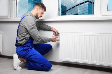 Professional plumber using pliers while preparing heating radiator for winter season in room