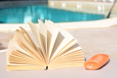 Open book on deck chair near swimming pool