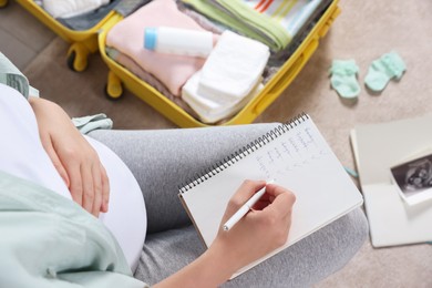 Pregnant woman preparing list of necessary items to bring into maternity hospital at home, top view