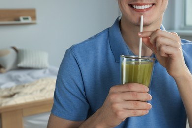 Young man drinking juice in bedroom, closeup