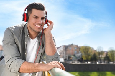 Handsome man with headphones listening to music outdoors on sunny day, space for text