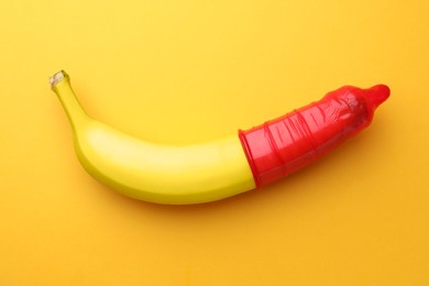Banana with condom on orange background, top view. Safe sex concept